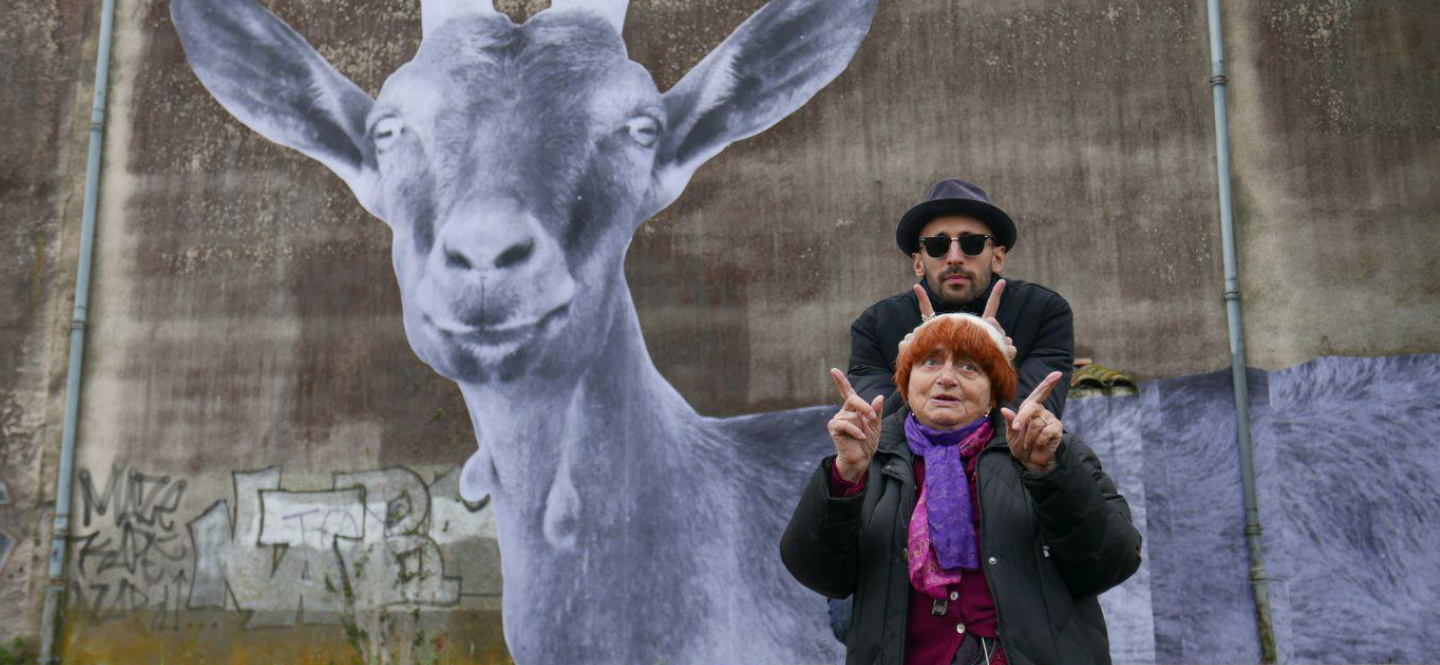 Na zdjęciu mężczyzna i kobieta na tle murary przedstawiającego ogromną kozę.