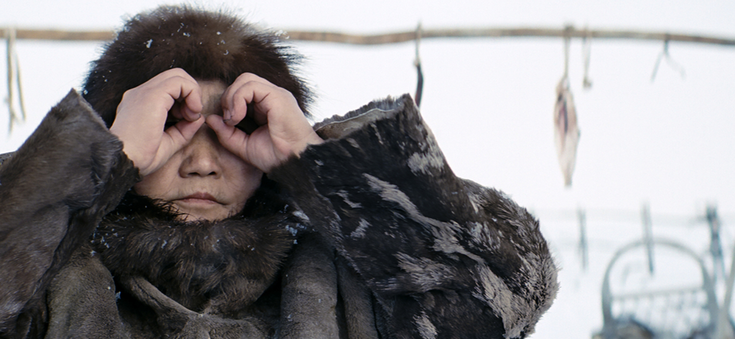 Kadr z filmu "Aga". Kobieta w futrzanej czapce i płaszczu przykłada ręce do oczu imitując lornetkę.