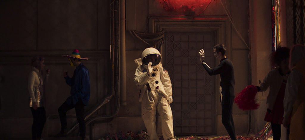 Kadr z filmu "Niepamięć". Grupa ludzi w kostiumach (kosmonauta, śmierć, meksykanin) stoi na ulicy