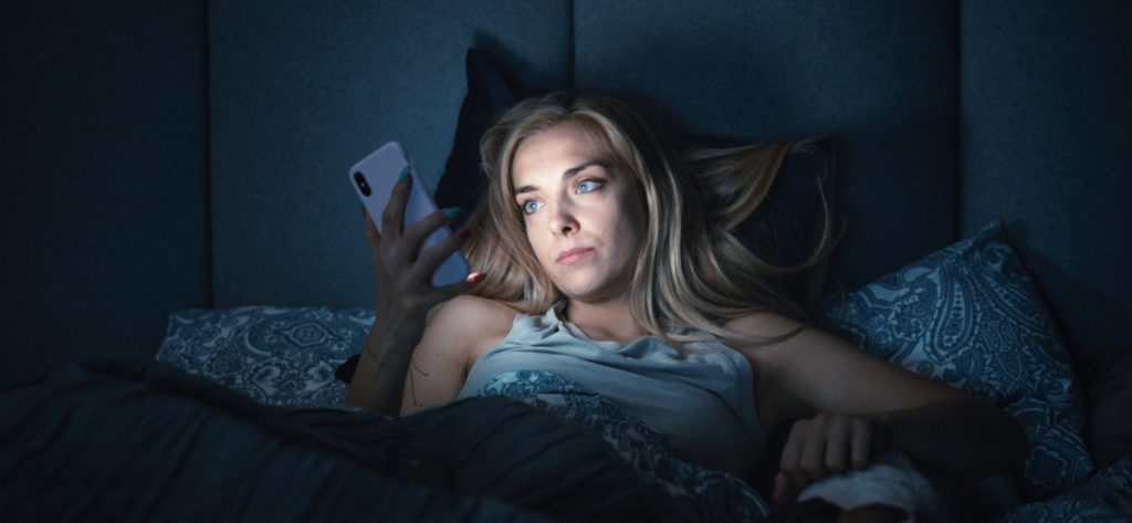 Kadr z filmu "Sweat". Kobieta w łóżku przegląda telefon.
