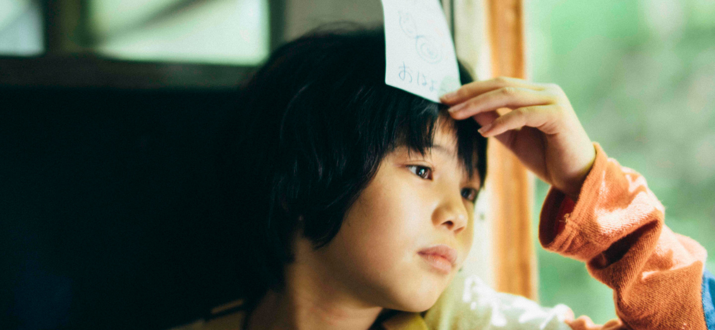 Na zdjęciu dziecko trzymające kartkę papieru przy czole