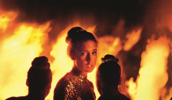 Na zdjęciu, stojąca tyłem do kadru, grupa kobiet wpatrzonych w palący się ogień. Jedna z nich jest odwrócona przodem do kadru.