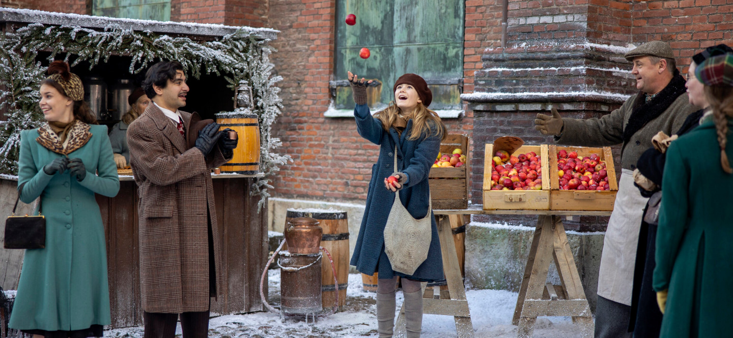 Na zdjęciu świąteczny jarmark, na którym stoi dziewczyna i żongluje jabłkami.