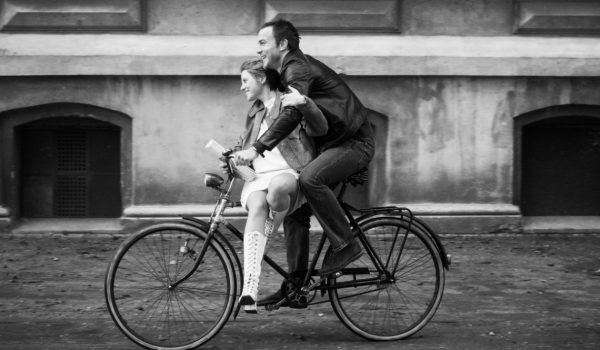 Na zdjęciu młody mężczyzna wiezie ulicą na ramie roweru dziewczynę